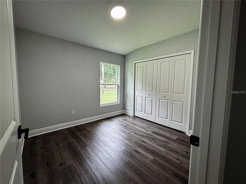 A bedroom with gray walls, dark wood-look flooring, a window, and white closet doors — 31 REDWOOD TRACK RUN, OCALA, FL