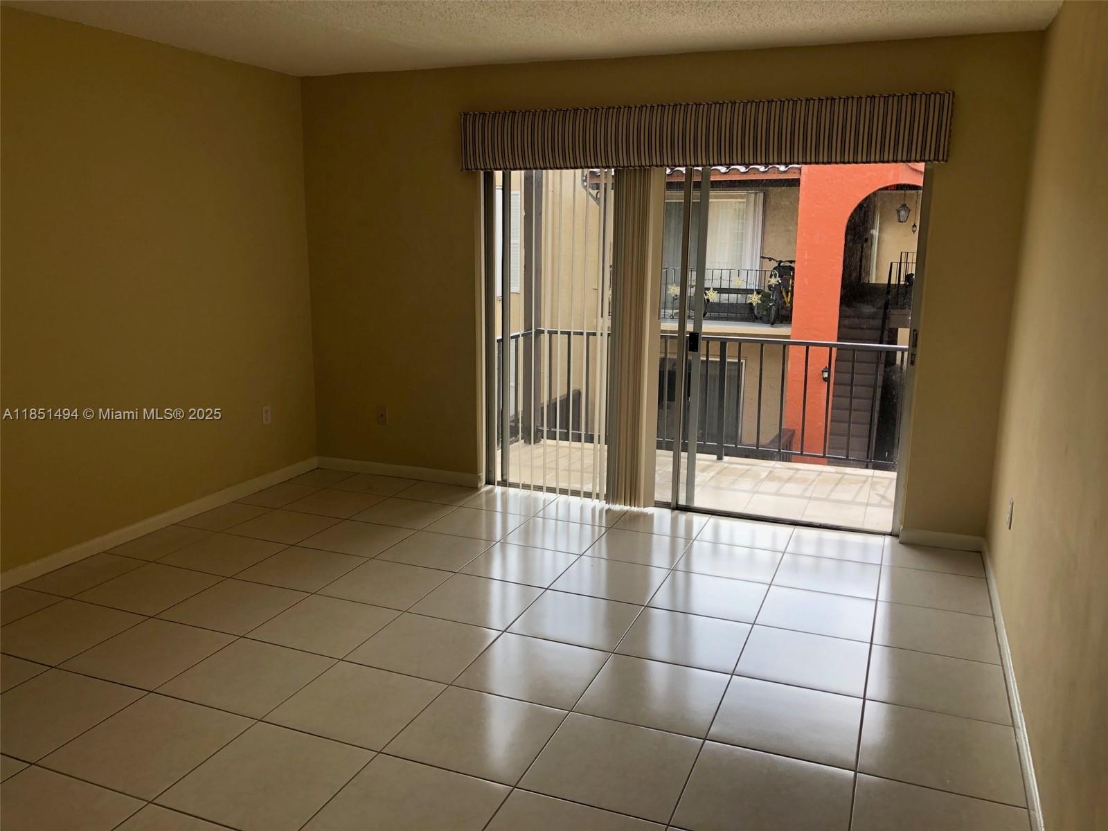 An empty room with beige tile flooring and sliding glass doors leading to a balcony — 10810 N Kendall Dr # 18, Miami FL 33176, MIAMI, FL