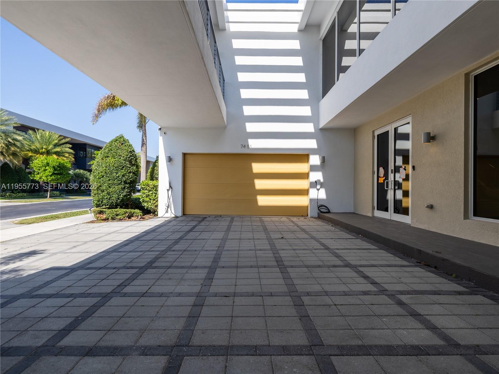 A paved driveway leads to a yellow garage door beneath a modern white building overhang — 7451 NW 103rd Ct # 0, Doral FL 33178, DORAL, FL