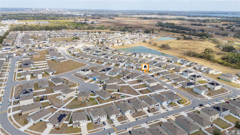 An aerial view shows a suburban neighborhood with numerous single-family homes and a retention pond — 740 SQUIRES GROVE DRIVE, WINTER HAVEN, FL