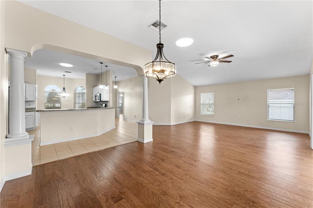 An open-concept living and dining area features hardwood floors, a kitchen island, and white columns — 16905 SE 93RD CUTHBERT CIRCLE, THE VILLAGES, FL