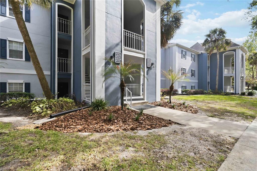 A multi-story apartment building exterior features blue siding, white trim, and a concrete walkway — 6206 BAYHILL LANE UNIT 6206, LONGWOOD, FL
