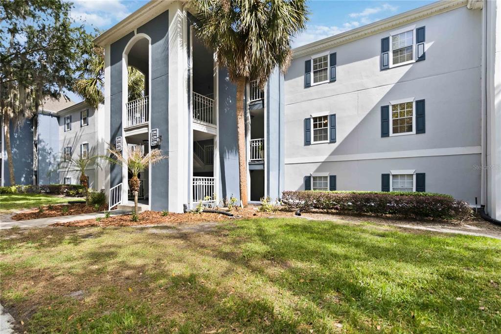 A three-story apartment building features light gray stucco walls, dark blue accents, and white railings — 6206 BAYHILL LANE UNIT 6206, LONGWOOD, FL