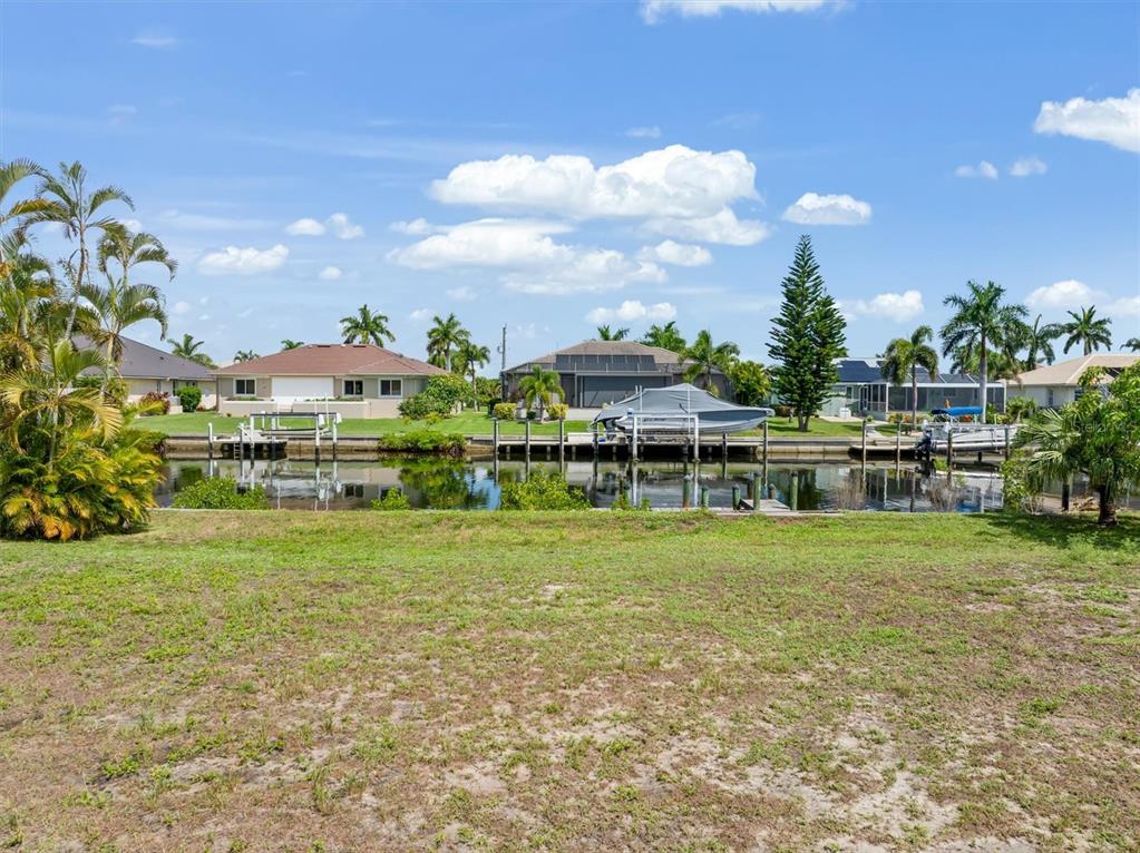 A grassy lot overlooks a canal with boat docks and houses in the background — 5439 RIVER BAY DRIVE, PUNTA GORDA, FL