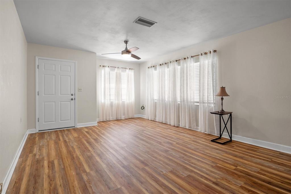 An empty room features light-colored walls, wood-look flooring, a ceiling fan, and white curtains — 1213 8TH STREET NW, WINTER HAVEN, FL