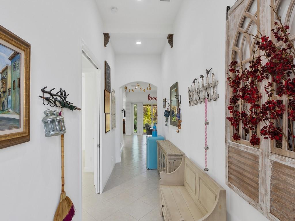 A bright hallway features white walls, tile flooring, a wooden bench, and decorative wall art — 8330 Summer Lake Drive, Vero Beach FL 32967, VERO BEACH, FL