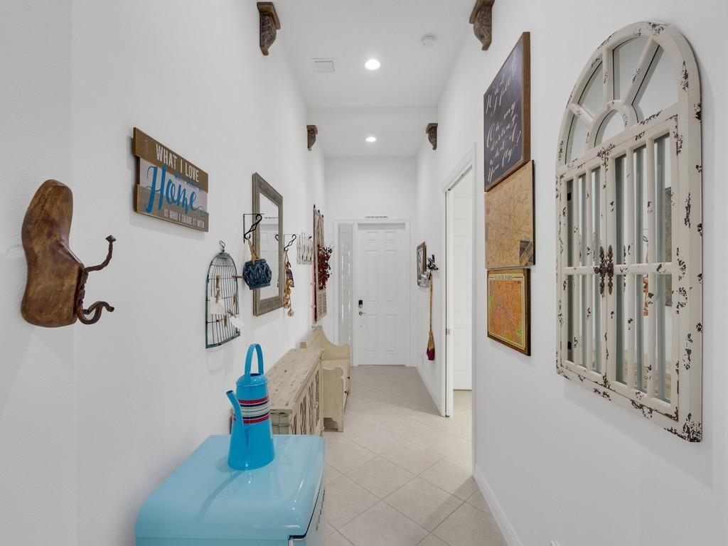 A bright hallway features white walls, tile flooring, decorative wall art, and a blue accent piece — 8330 Summer Lake Drive, Vero Beach FL 32967, VERO BEACH, FL