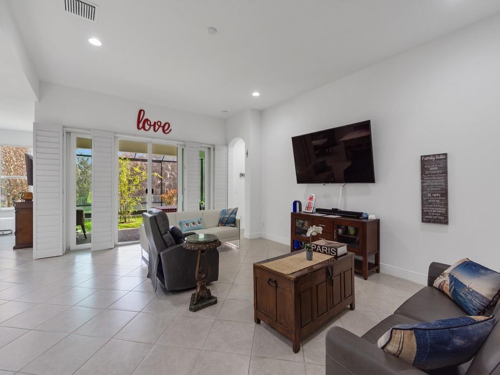 A living room features light tile floors, a wall-mounted television, and sliding glass patio doors — 8330 Summer Lake Drive, Vero Beach FL 32967, VERO BEACH, FL