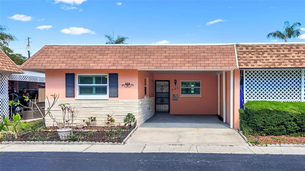 A single-story house with a peach exterior, a carport, and a brown shingled roof — 325 SKY LOCH DRIVE W, DUNEDIN, FL