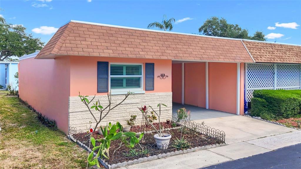 A peach-colored single-story house features a brown shingled mansard roof and a front carport — 325 SKY LOCH DRIVE W, DUNEDIN, FL