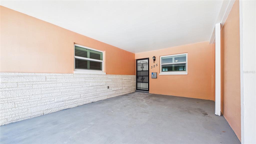 A covered carport features peach-colored walls, a white stone-textured lower facade, and a security door — 325 SKY LOCH DRIVE W, DUNEDIN, FL