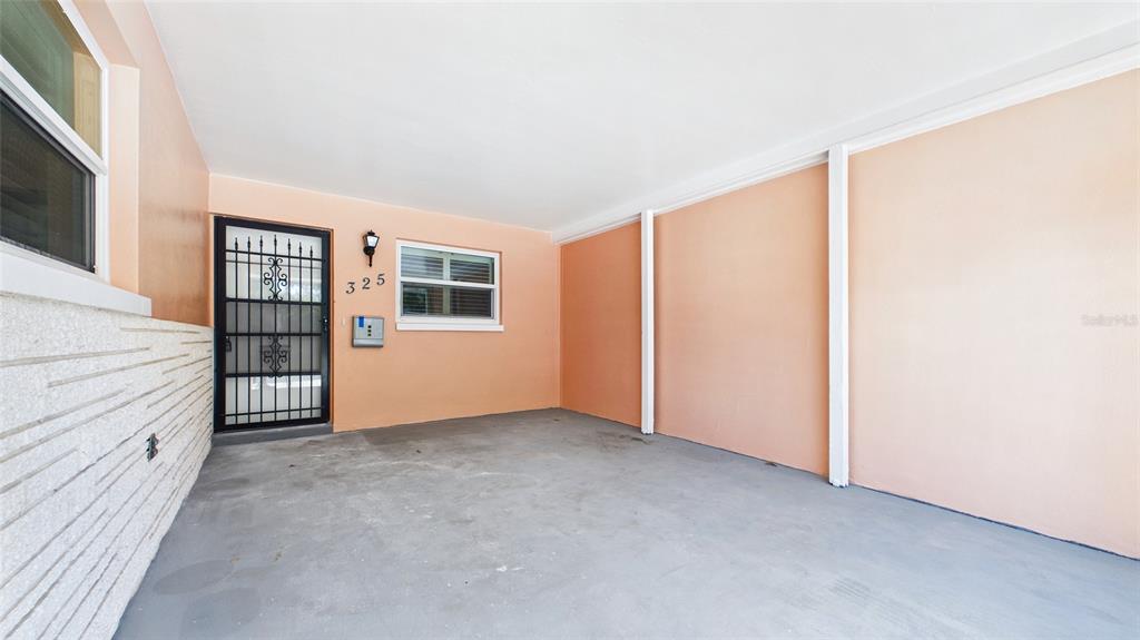A covered carport with peach-colored walls, a concrete floor, and a security-screened front door — 325 SKY LOCH DRIVE W, DUNEDIN, FL