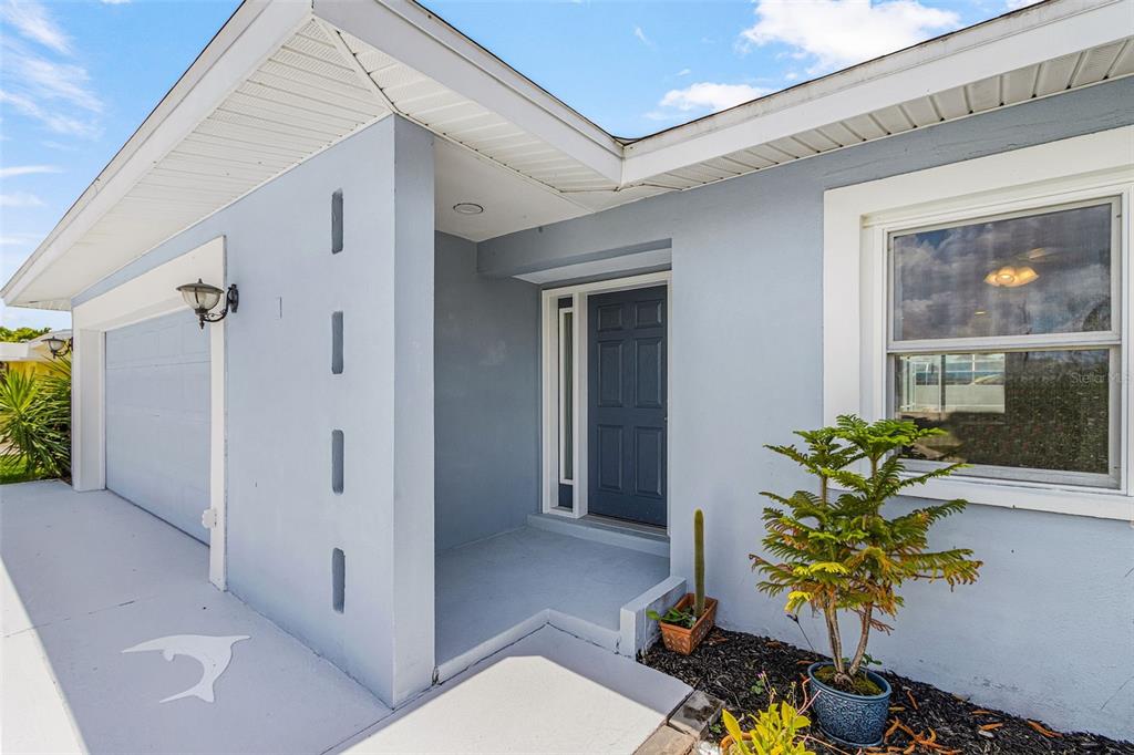 A light blue house exterior features a dark front door, a garage, and a small tree — 1320 SE 26TH TERRACE, CAPE CORAL, FL