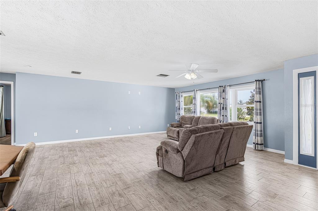 A living room features light blue walls, wood-look tile flooring, and a brown reclining sofa — 1320 SE 26TH TERRACE, CAPE CORAL, FL