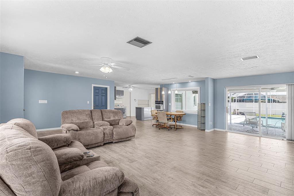 A living room with light blue walls, wood-look tile flooring, and a sliding glass door — 1320 SE 26TH TERRACE, CAPE CORAL, FL