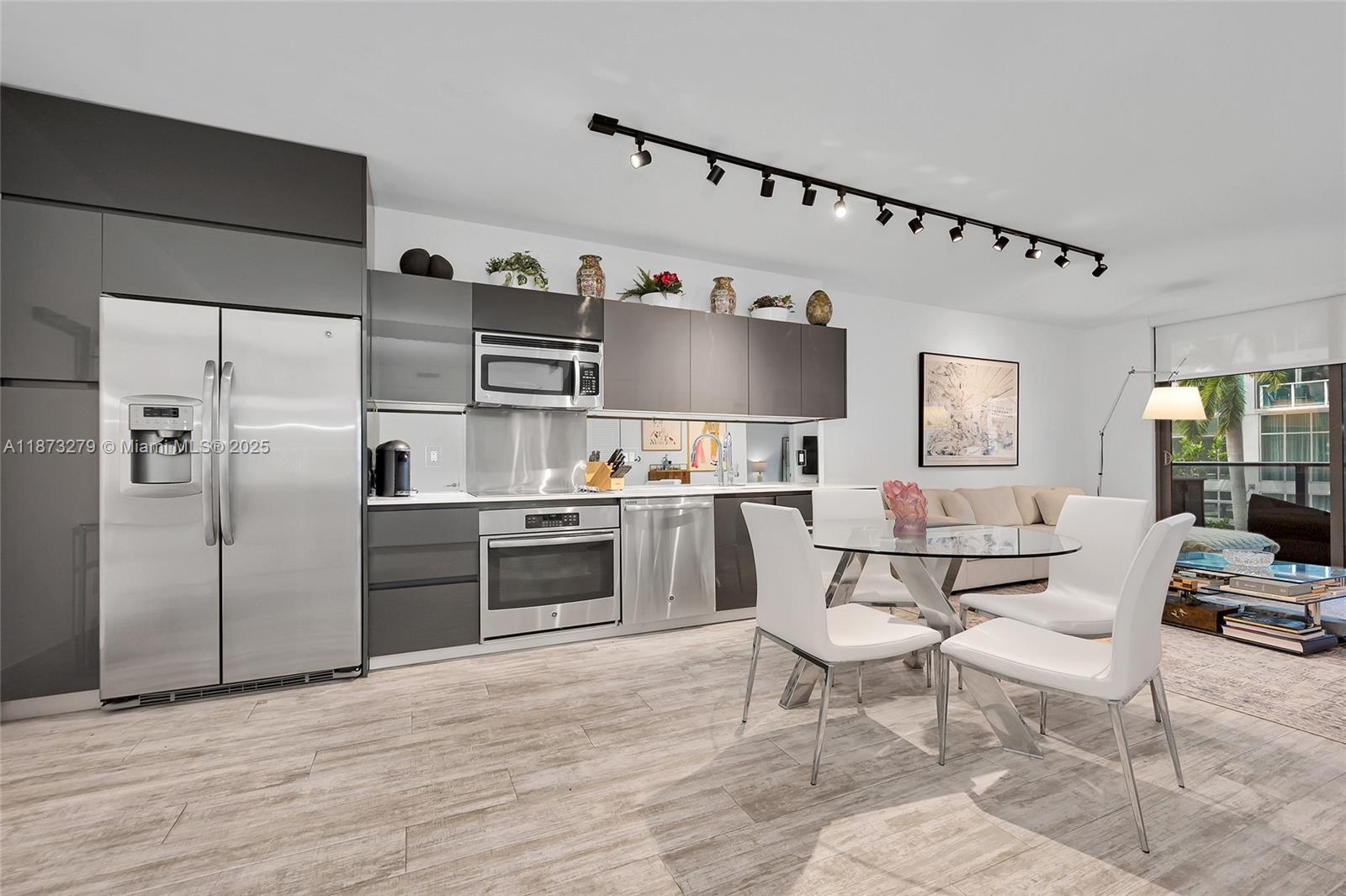 A modern kitchen and dining area features gray cabinetry, stainless steel appliances, and white chairs — 31 SE 6th St # 304, Miami FL 33131, MIAMI, FL