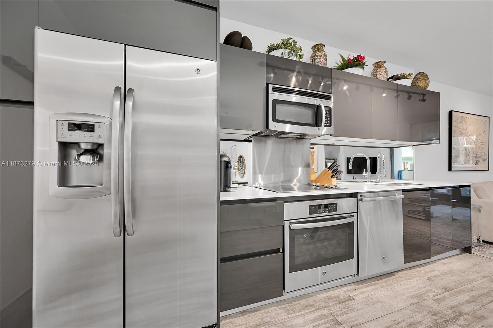 A modern kitchen features stainless steel appliances, glossy gray cabinetry, and a mirrored backsplash — 31 SE 6th St # 304, Miami FL 33131, MIAMI, FL