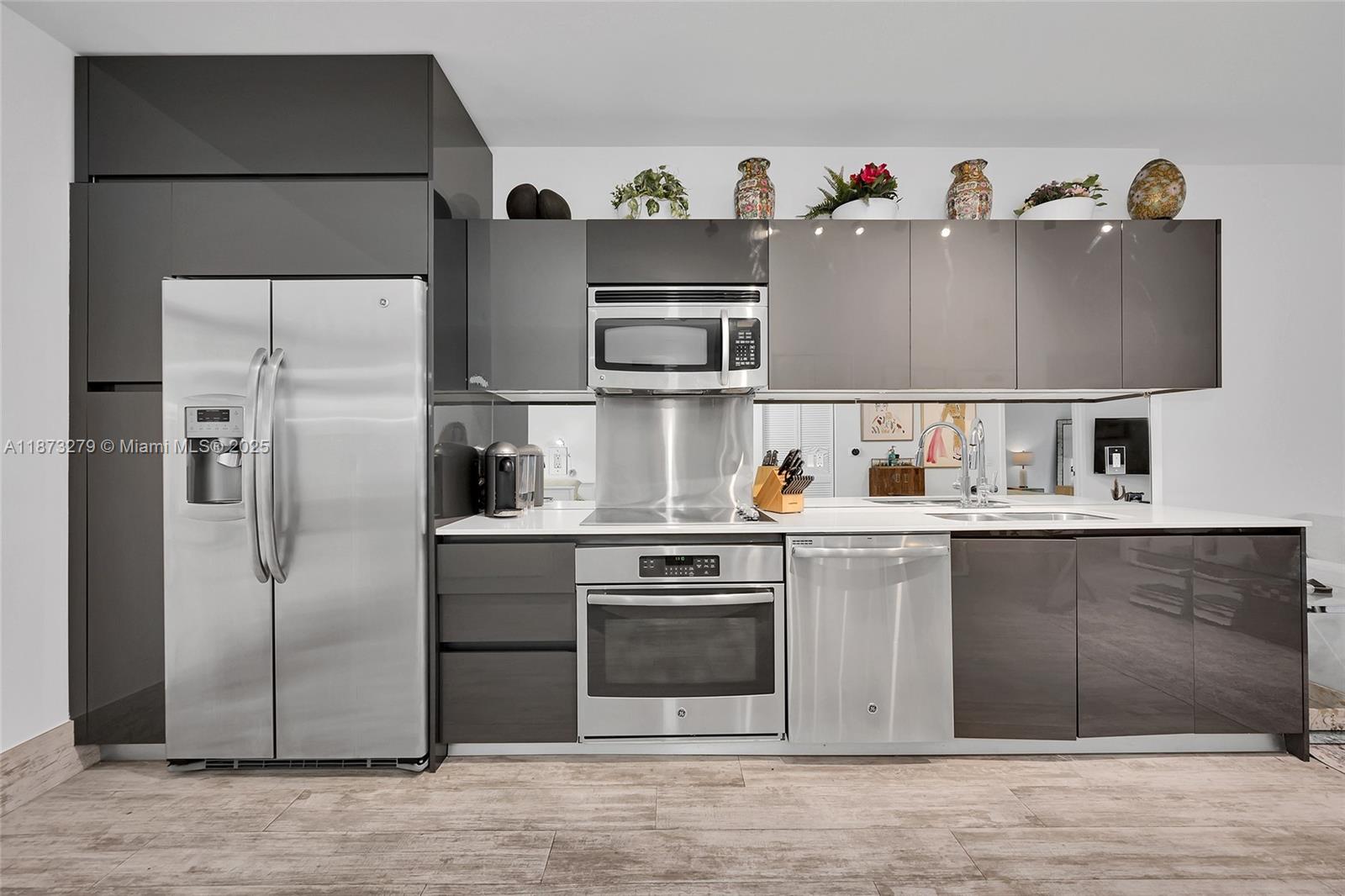 A modern kitchen features dark gray cabinetry, stainless steel appliances, and a mirrored backsplash — 31 SE 6th St # 304, Miami FL 33131, MIAMI, FL
