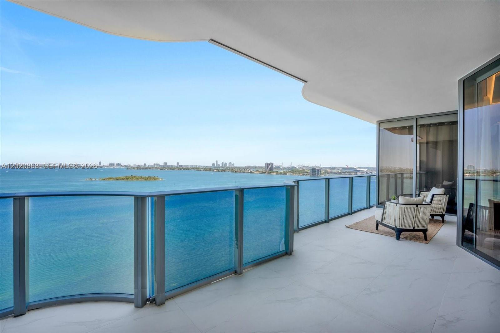 A spacious balcony features white tile flooring, a glass railing, and panoramic bay views — 700 NE 24th St # 1602, Miami FL 33137, MIAMI, FL