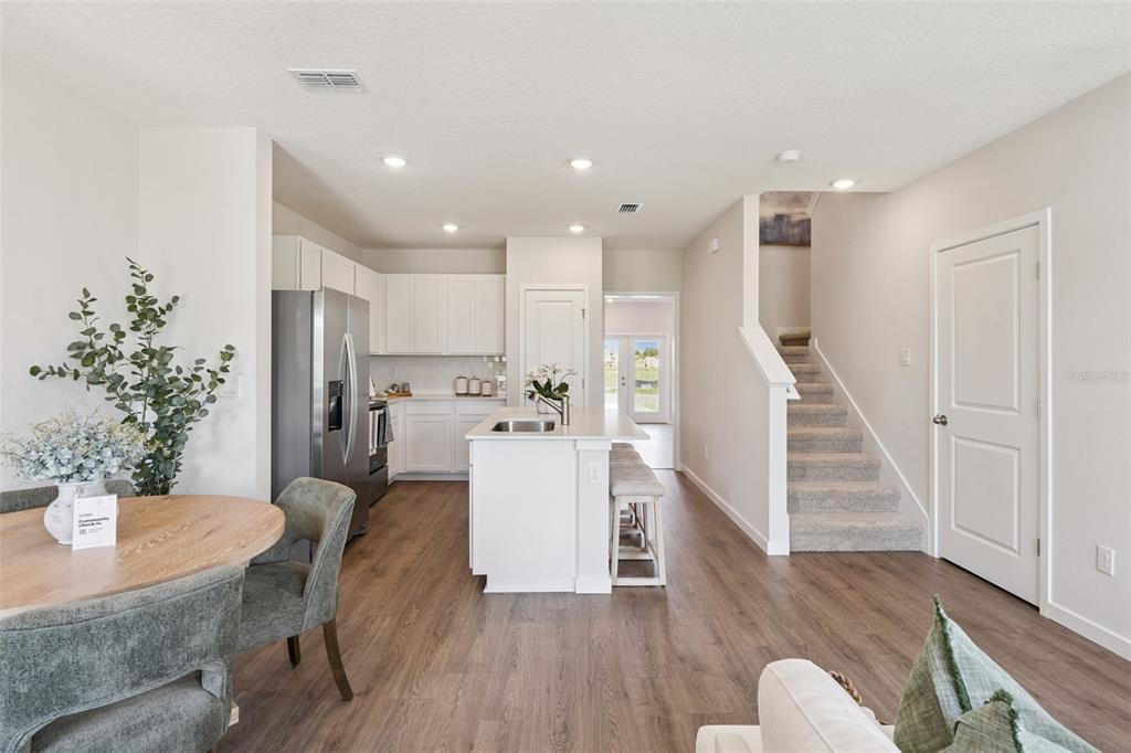 A kitchen with white cabinets, a central island, and wood-look flooring opens to a staircase — 2253 RITA LANE, KISSIMMEE, FL