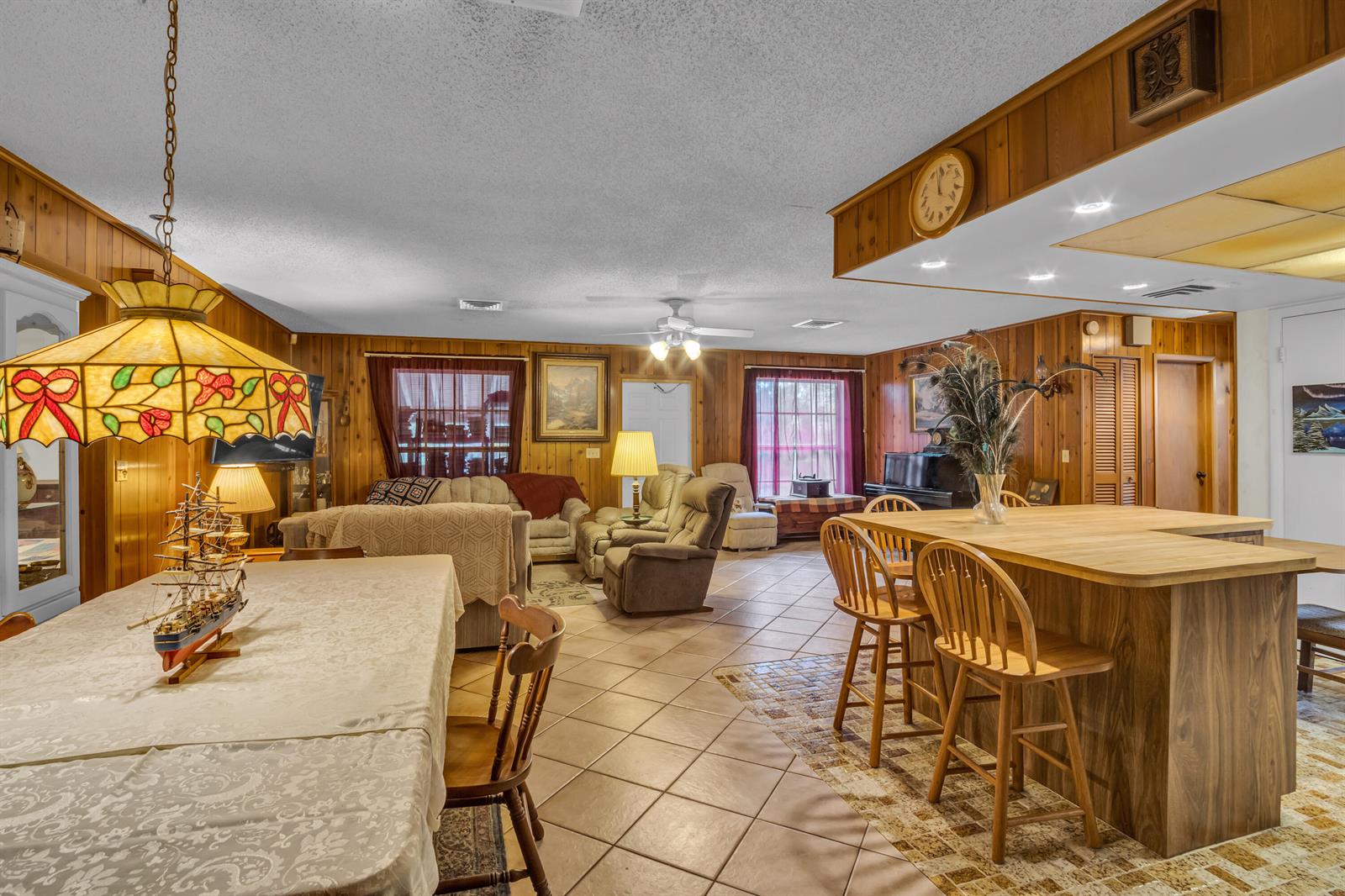 A dining and living area features wood-paneled walls, tile flooring, and a kitchen island — 14181 35th Place N, FL 33470, FL