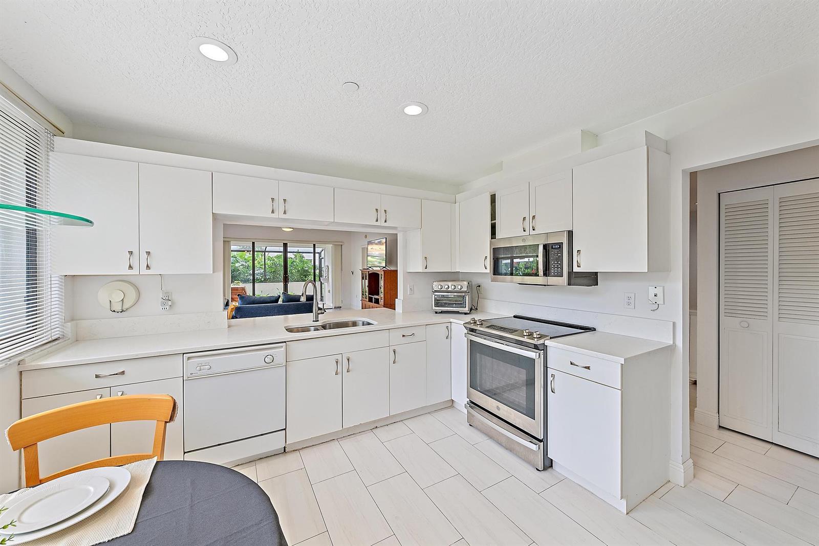 A white kitchen features stainless steel appliances, white cabinetry, and a pass-through window to outdoors — 811 Oak Harbour Drive, Juno Beach FL 33408, JUNO BEACH, FL