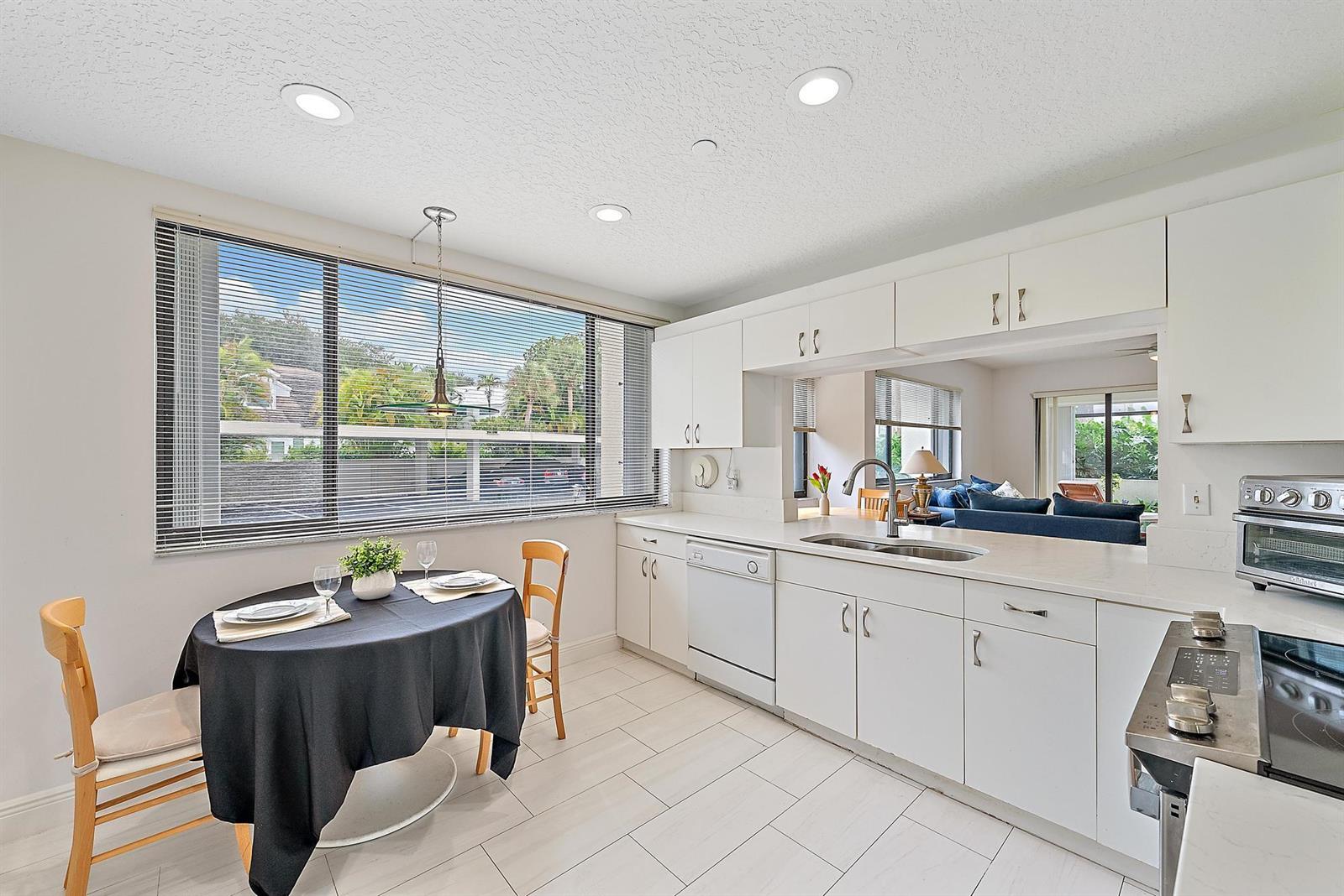 A bright kitchen features white cabinetry, light tile flooring, and a small dining table — 811 Oak Harbour Drive, Juno Beach FL 33408, JUNO BEACH, FL