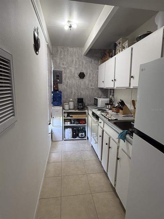 A narrow galley kitchen features white cabinets, tile flooring, and a stainless steel sink — 4719 CLUB CIRCLE, LAKE WALES, FL