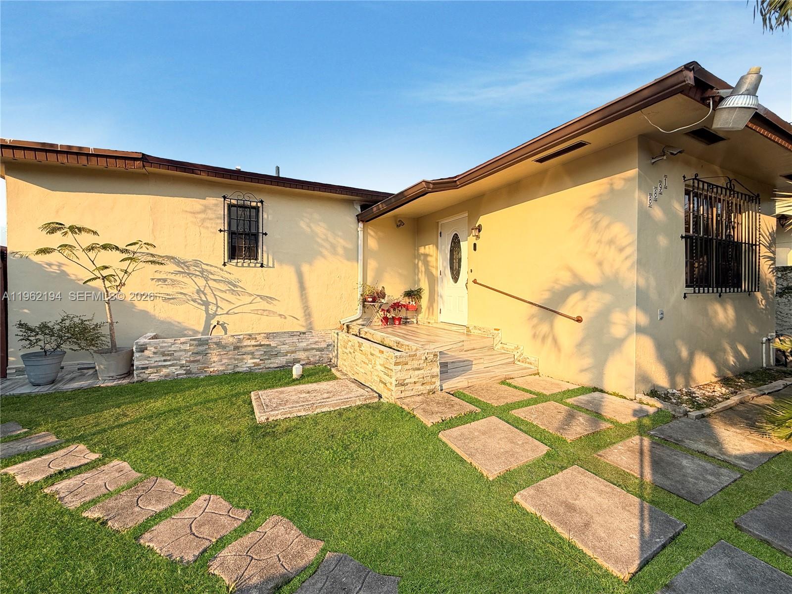 The exterior of a beige house features a stone-accented entryway, a lawn, and stone pavers — 8891 SW 28th St, Miami FL 33165, MIAMI, FL