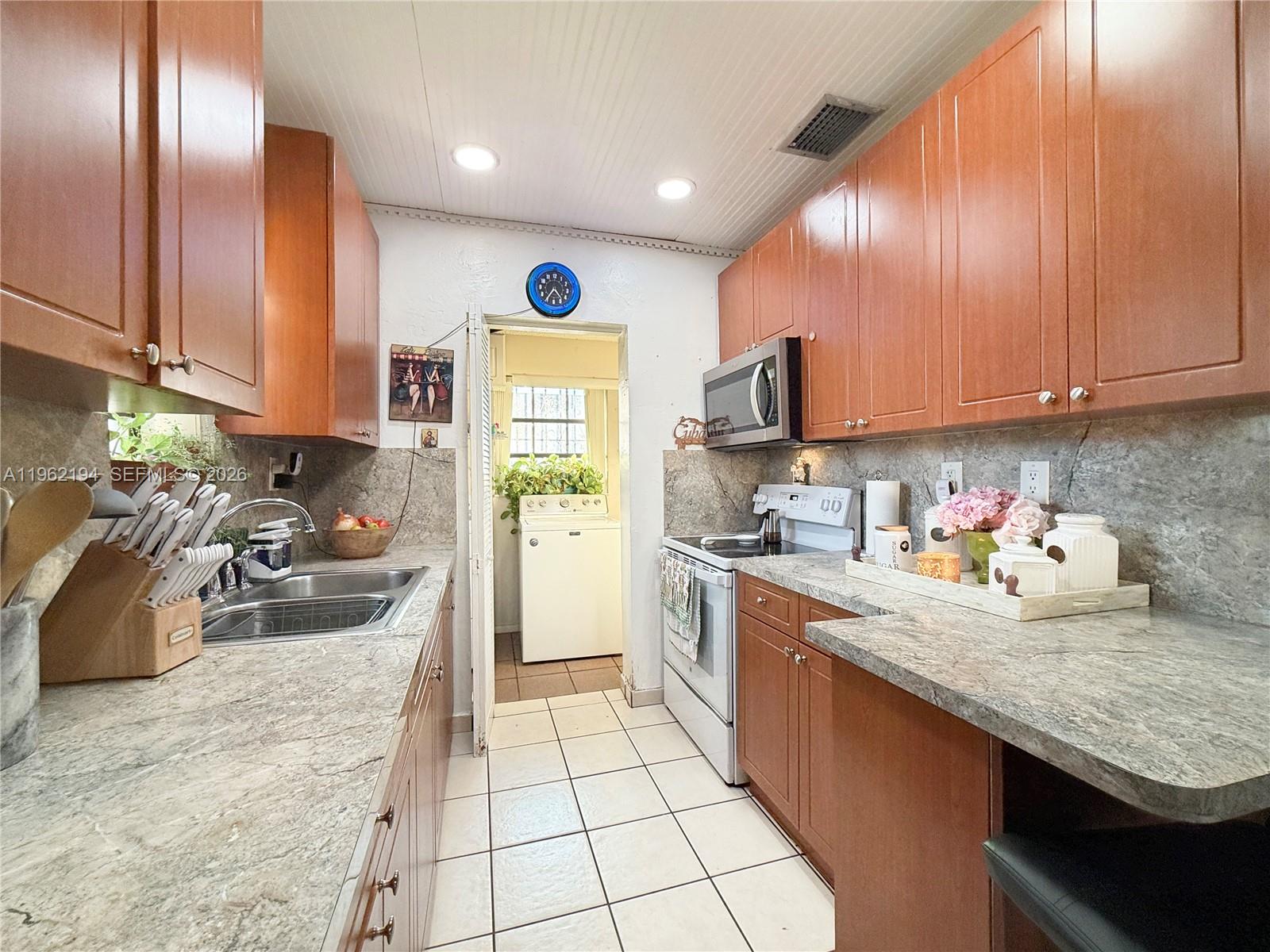 A galley kitchen features wood cabinets, stone-look countertops, tile flooring, and an adjacent laundry room — 8891 SW 28th St, Miami FL 33165, MIAMI, FL