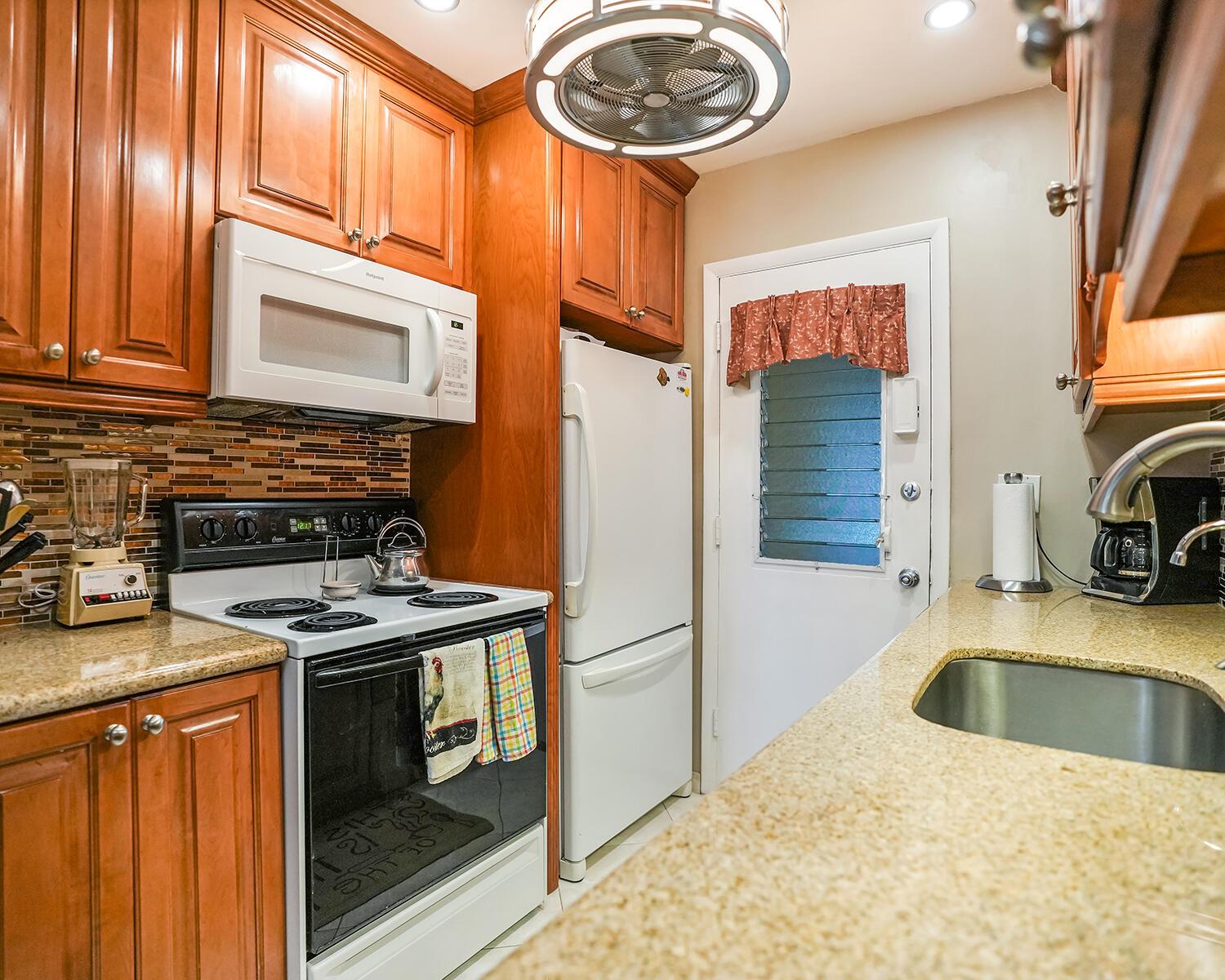 A kitchen features wood cabinets, granite countertops, white appliances, and a ceiling fan — 16801 NE 13th Avenue # 308, Miami FL 33162, MIAMI, FL