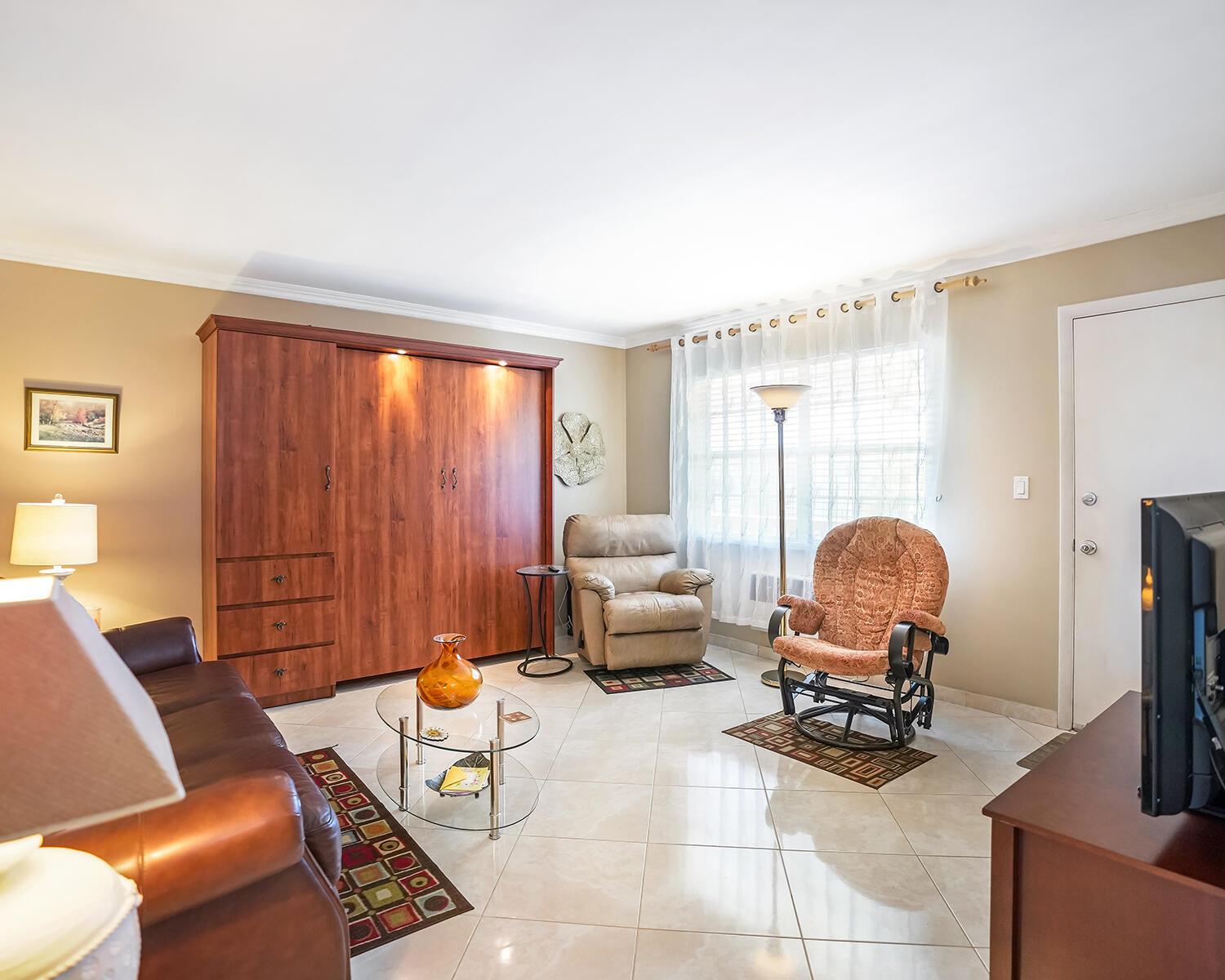 A living room features a large wooden wall unit, tiled floors, and two comfortable armchairs — 16801 NE 13th Avenue # 308, Miami FL 33162, MIAMI, FL