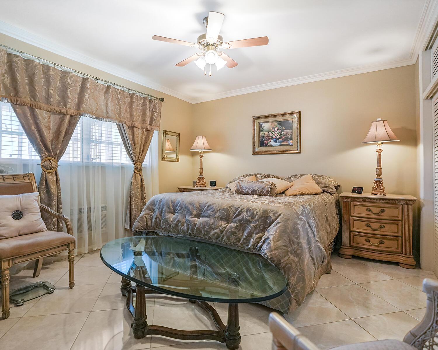A bedroom features a bed with patterned bedding, two nightstands with lamps, and a glass table — 16801 NE 13th Avenue # 308, Miami FL 33162, MIAMI, FL