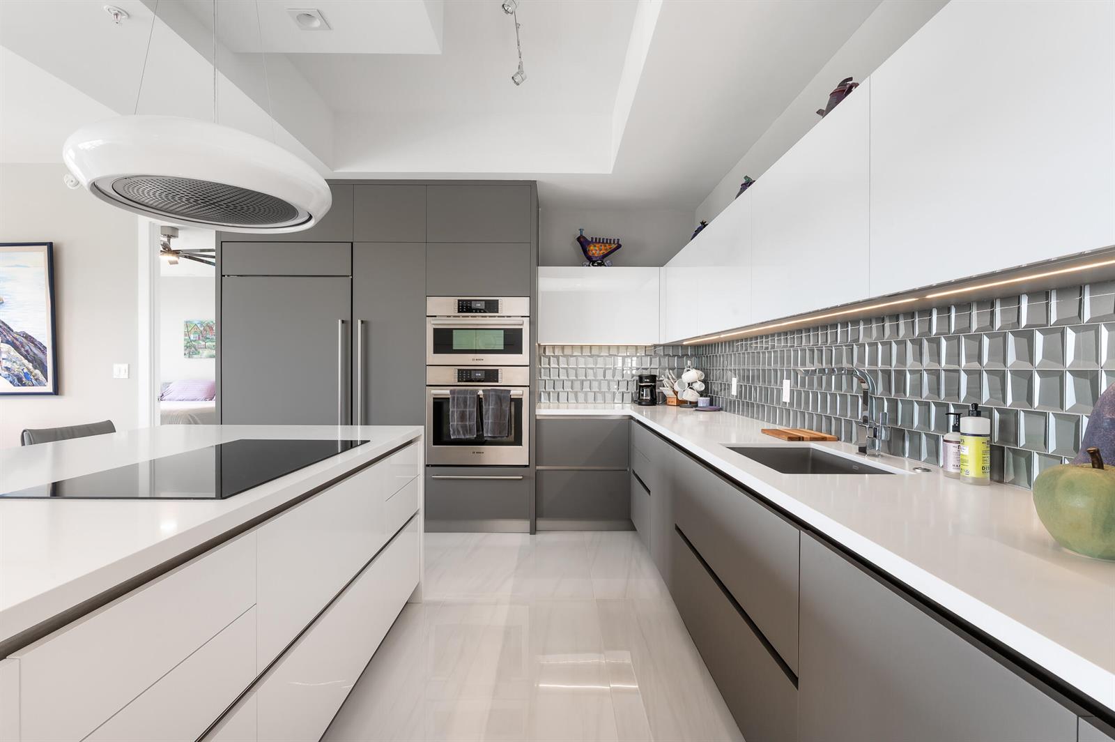 A modern kitchen features white and gray cabinetry, a large island, and a tiled backsplash — 155 E Boca Raton Road # 1107, Boca Raton FL 33432, BOCA RATON, FL
