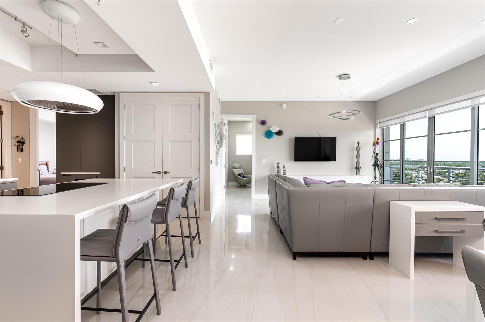 A modern open-concept living room and kitchen featuring gray leather furniture and white tile flooring — 155 E Boca Raton Road # 1107, Boca Raton FL 33432, BOCA RATON, FL