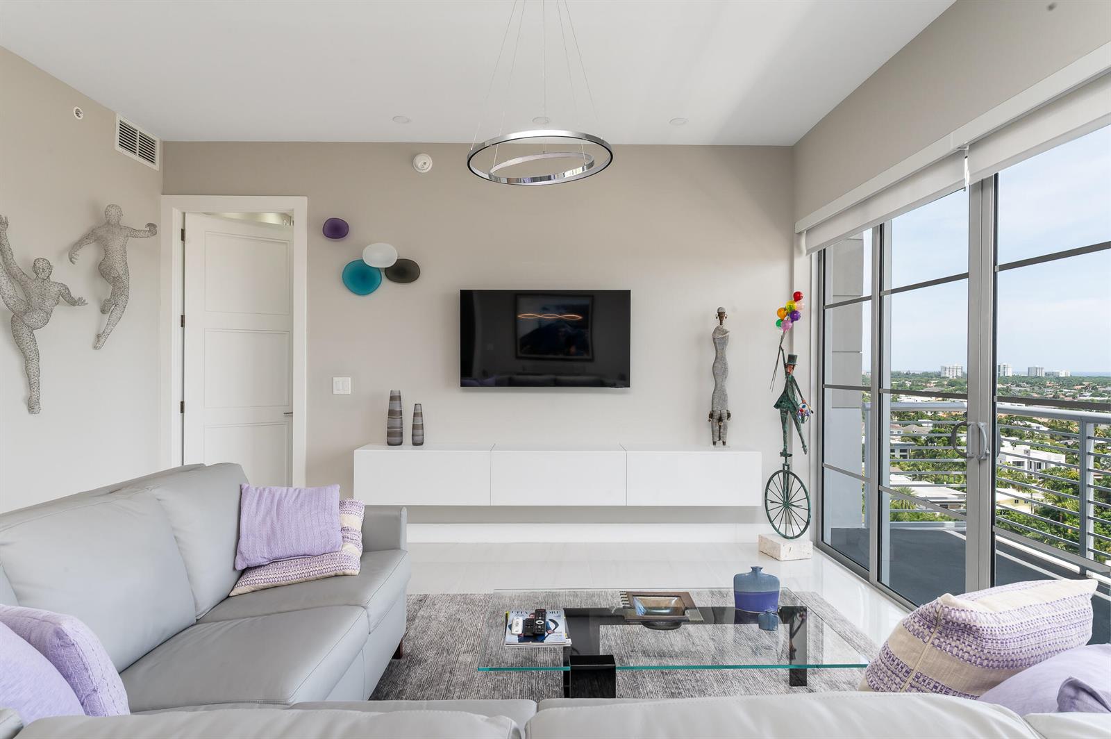 A modern living room features a wall-mounted television, floating white console, and floor-to-ceiling windows — 155 E Boca Raton Road # 1107, Boca Raton FL 33432, BOCA RATON, FL