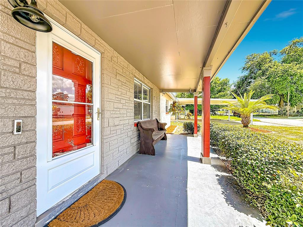 A covered front porch features a red door, a wooden bench, and light-colored brick siding — 2019 HESS DRIVE, HOLIDAY, FL