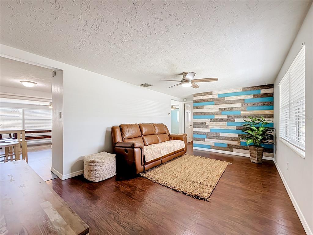 A living room features a brown leather sofa, a wood-plank accent wall, and wood flooring — 2019 HESS DRIVE, HOLIDAY, FL