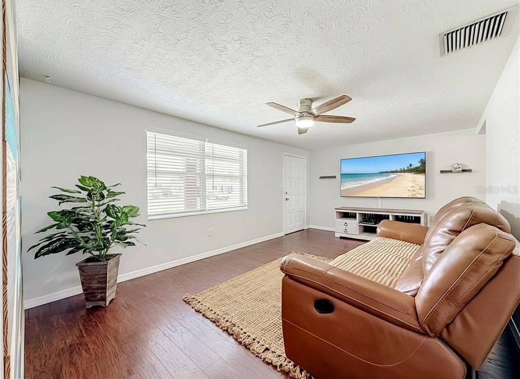 A living room features wood-look flooring, a brown leather sofa, a ceiling fan, and a television — 2019 HESS DRIVE, HOLIDAY, FL