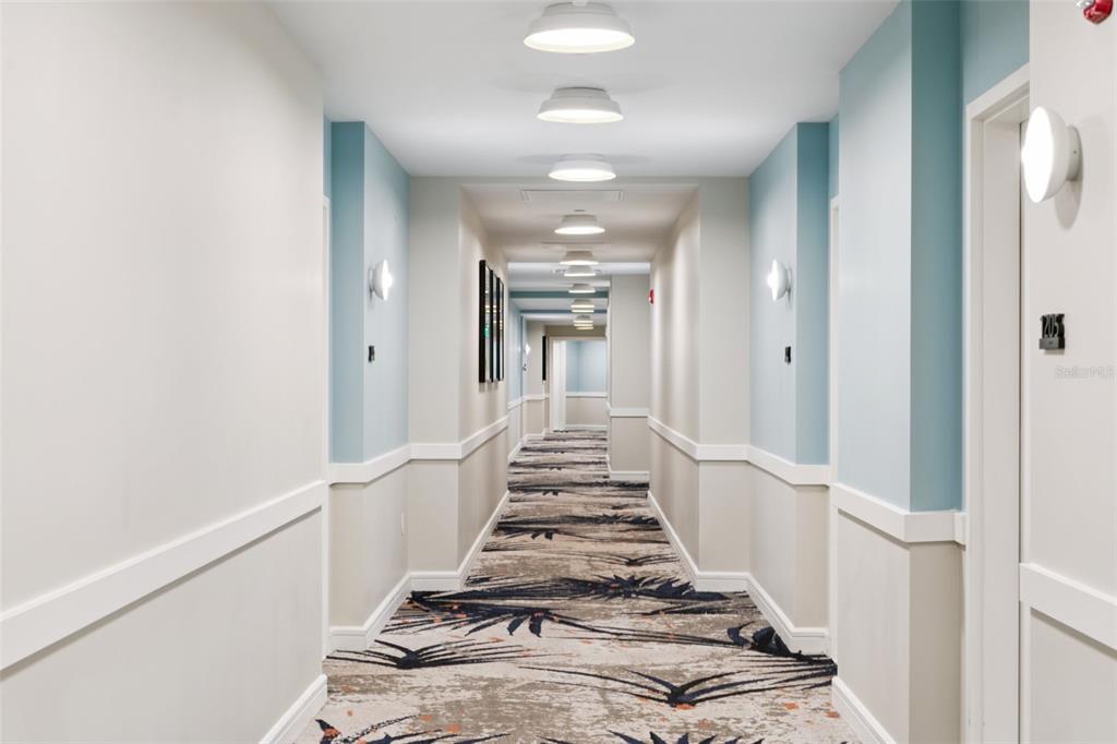 A long hotel hallway features patterned carpet, light blue and beige walls, and recessed lighting — 3151 SUNSET WALK DRIVE UNIT 1202, KISSIMMEE, FL