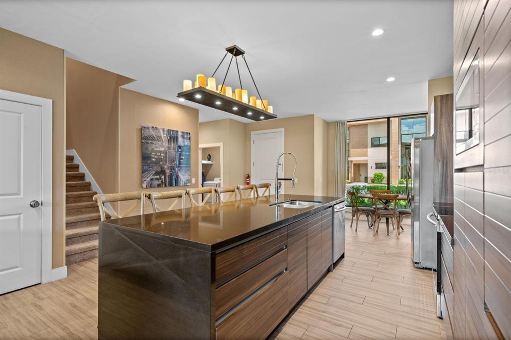 A modern kitchen features a dark stone island, wood-grain cabinets, and a candle-style chandelier — 3092 ROCKEFELLER WAY, KISSIMMEE, FL