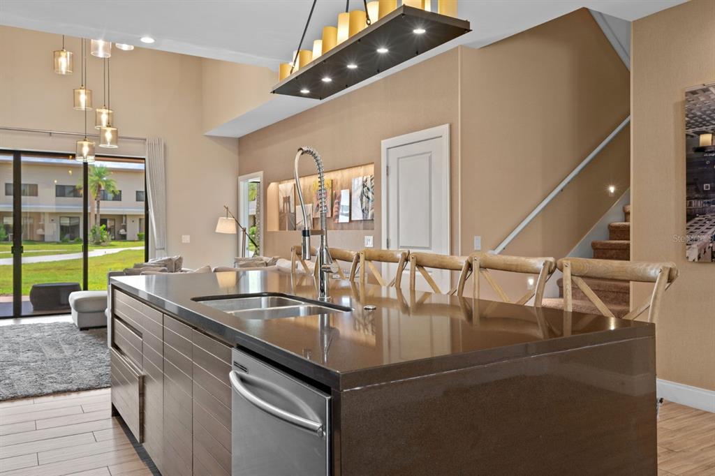 A kitchen island with a dark countertop and stainless steel dishwasher faces a living area — 3092 ROCKEFELLER WAY, KISSIMMEE, FL