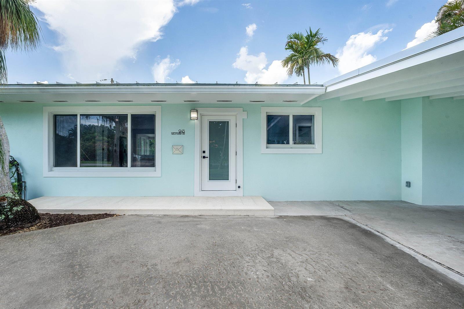 A light blue exterior house features a white front door, large windows, and a carport — 945 Westwind Drive, North Palm Beach FL 33408, NORTH PALM BEACH, FL