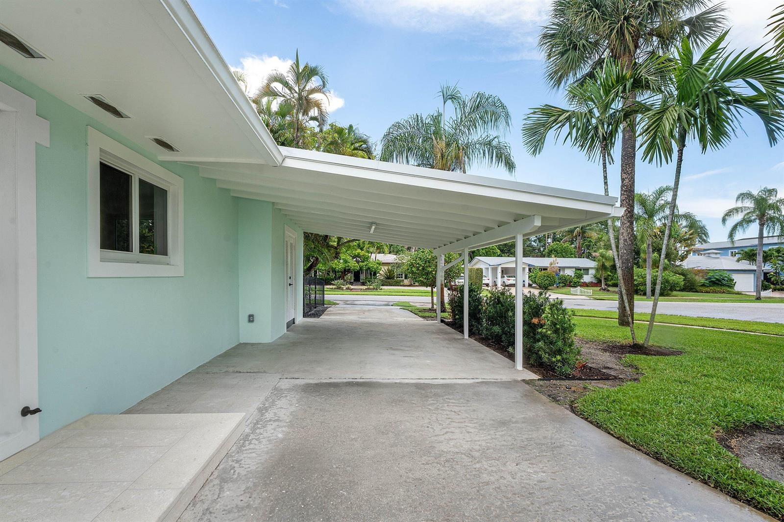 A light green house features a concrete driveway covered by a white metal carport — 945 Westwind Drive, North Palm Beach FL 33408, NORTH PALM BEACH, FL