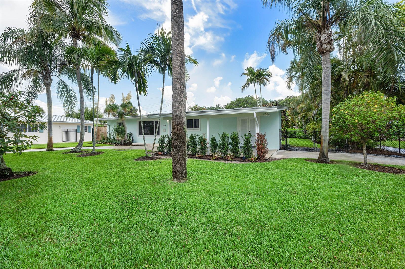 A light blue, single-story house sits behind a large green lawn with several palm trees — 945 Westwind Drive, North Palm Beach FL 33408, NORTH PALM BEACH, FL