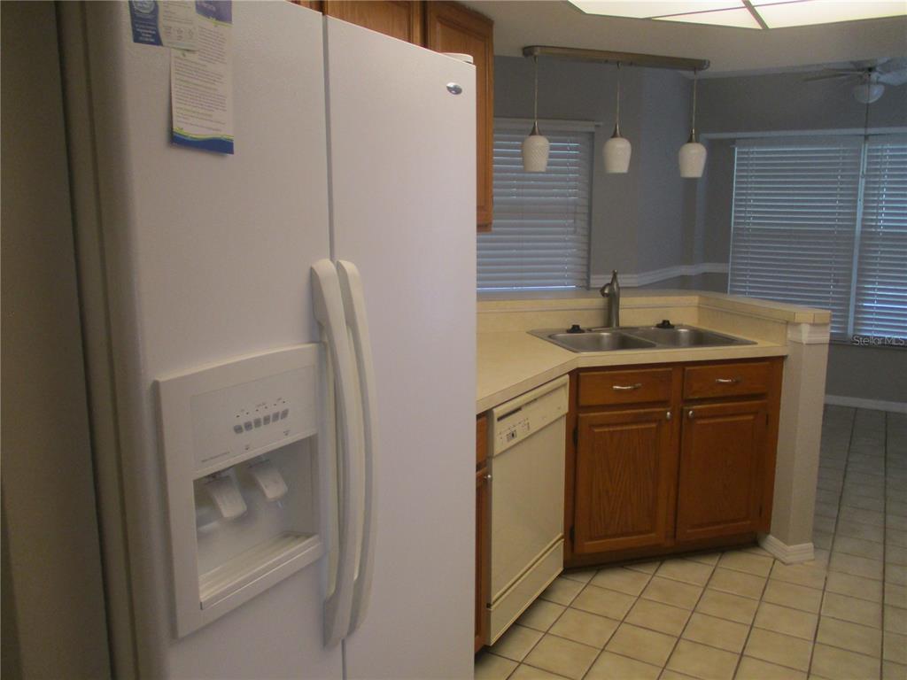 A kitchen features white appliances, wood cabinets, a corner sink, and tile flooring — 209 N BROCKFIELD DRIVE, SUN CITY CENTER, FL