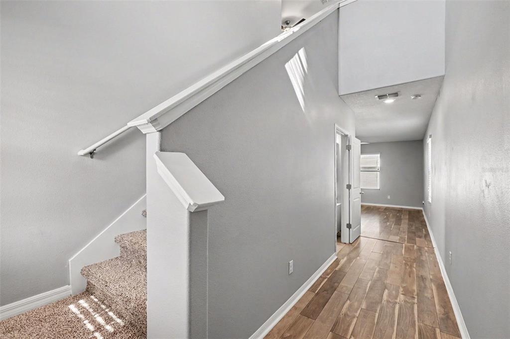 A hallway with wood-look flooring leads to a room, featuring a carpeted staircase on the left — 14803 EMERALD LANDING PLACE, WIMAUMA, FL