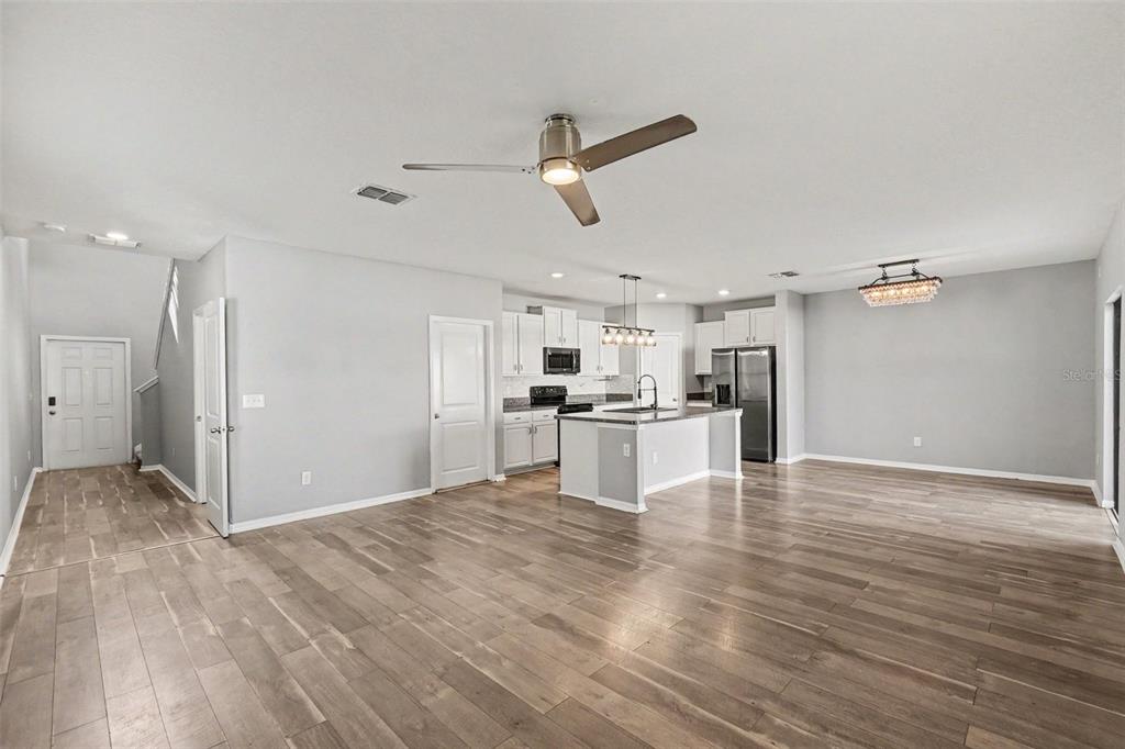 An open-concept kitchen and living area features light wood flooring, white cabinetry, and a ceiling fan — 14803 EMERALD LANDING PLACE, WIMAUMA, FL