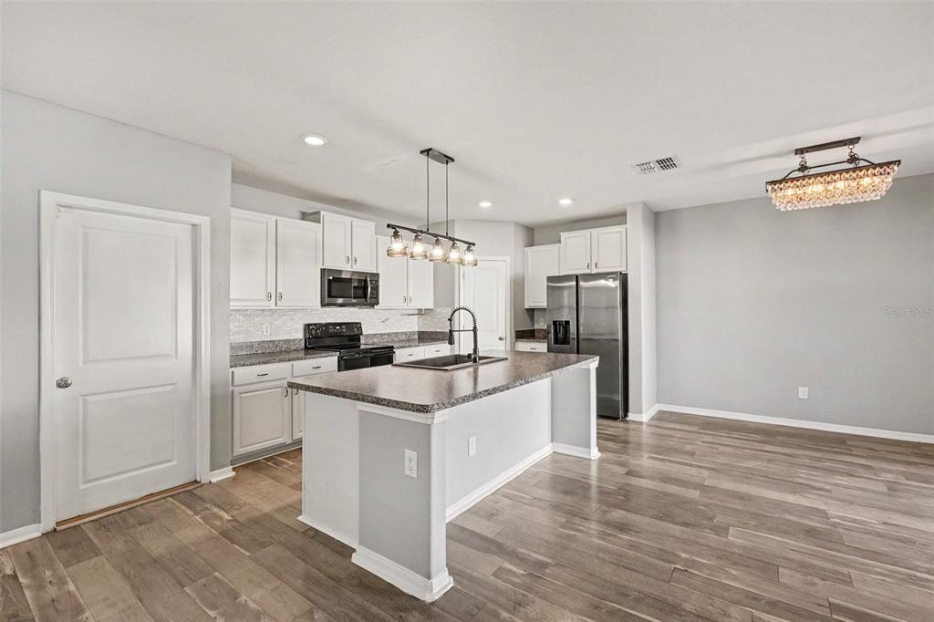 A kitchen features white cabinets, a central island with a sink, and wood-look flooring — 14803 EMERALD LANDING PLACE, WIMAUMA, FL