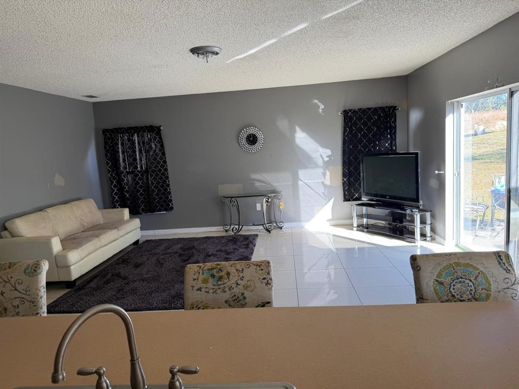 A living room features a white sofa, a dark area rug, and a glass television stand — 1403 KISSIMMEE COURT, KISSIMMEE, FL